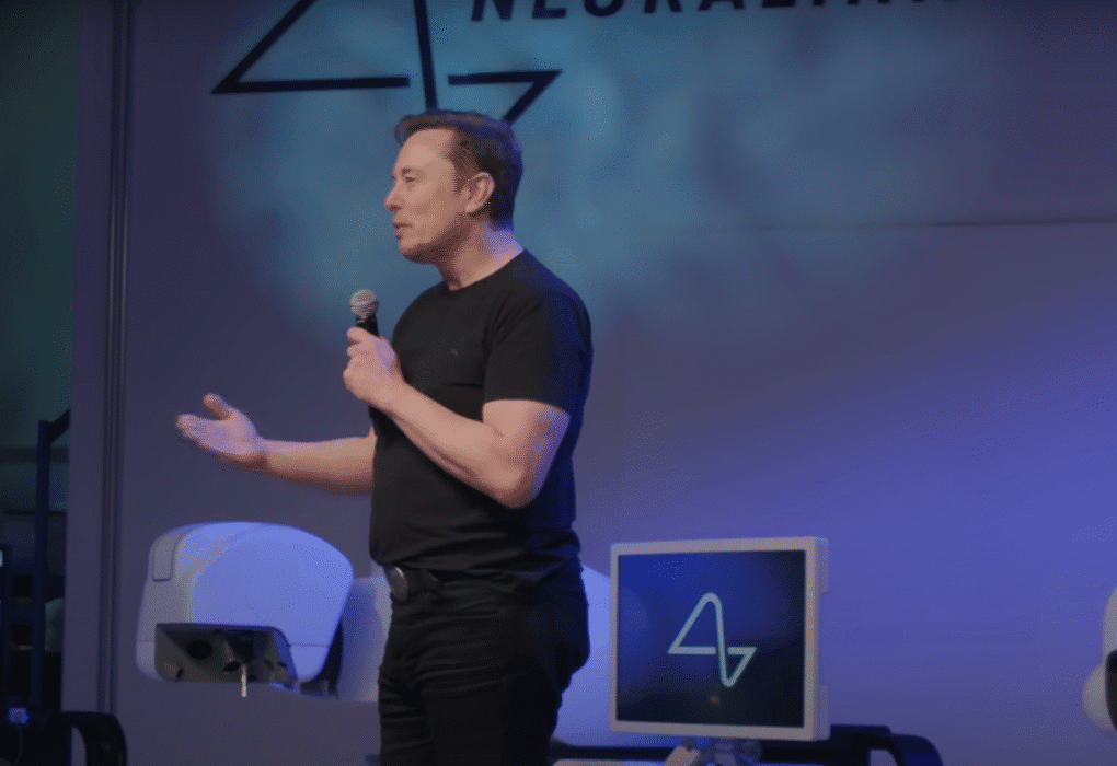 Elon Musk speaking on stage with Neuralink logo displayed behind him at the Neuralink update 2025 event