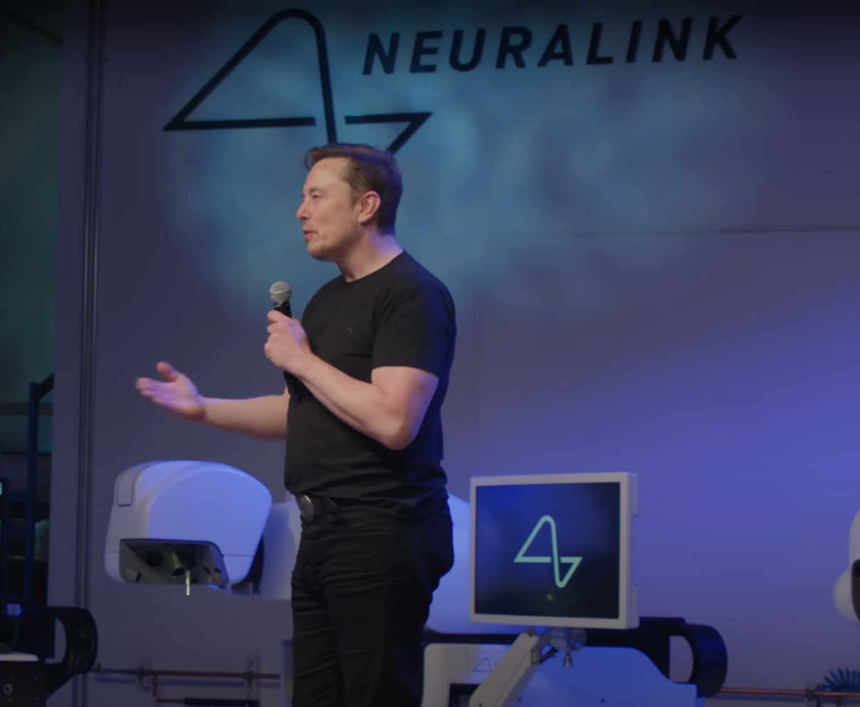 Elon Musk speaking on stage with Neuralink logo displayed behind him at the Neuralink update 2025 event